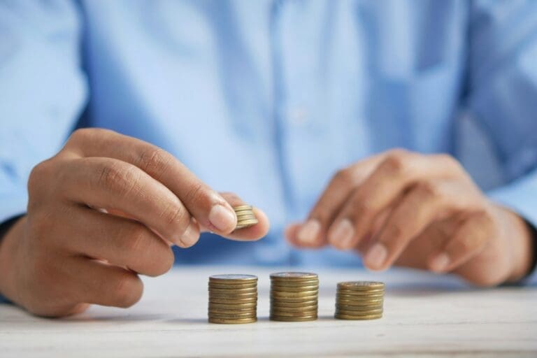 A pair of hands stack gold coins, the person has a blue shirt on.