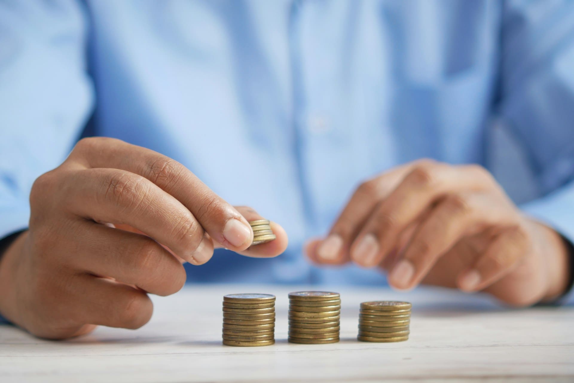 A pair of hands stack gold coins, the person has a blue shirt on.